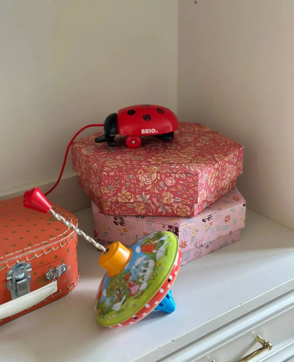 Alison Hexagon silk boxes by Sissel Edelbo in pink floral pattern, styled on a shelf with BRIO ladybug and vintage toy top