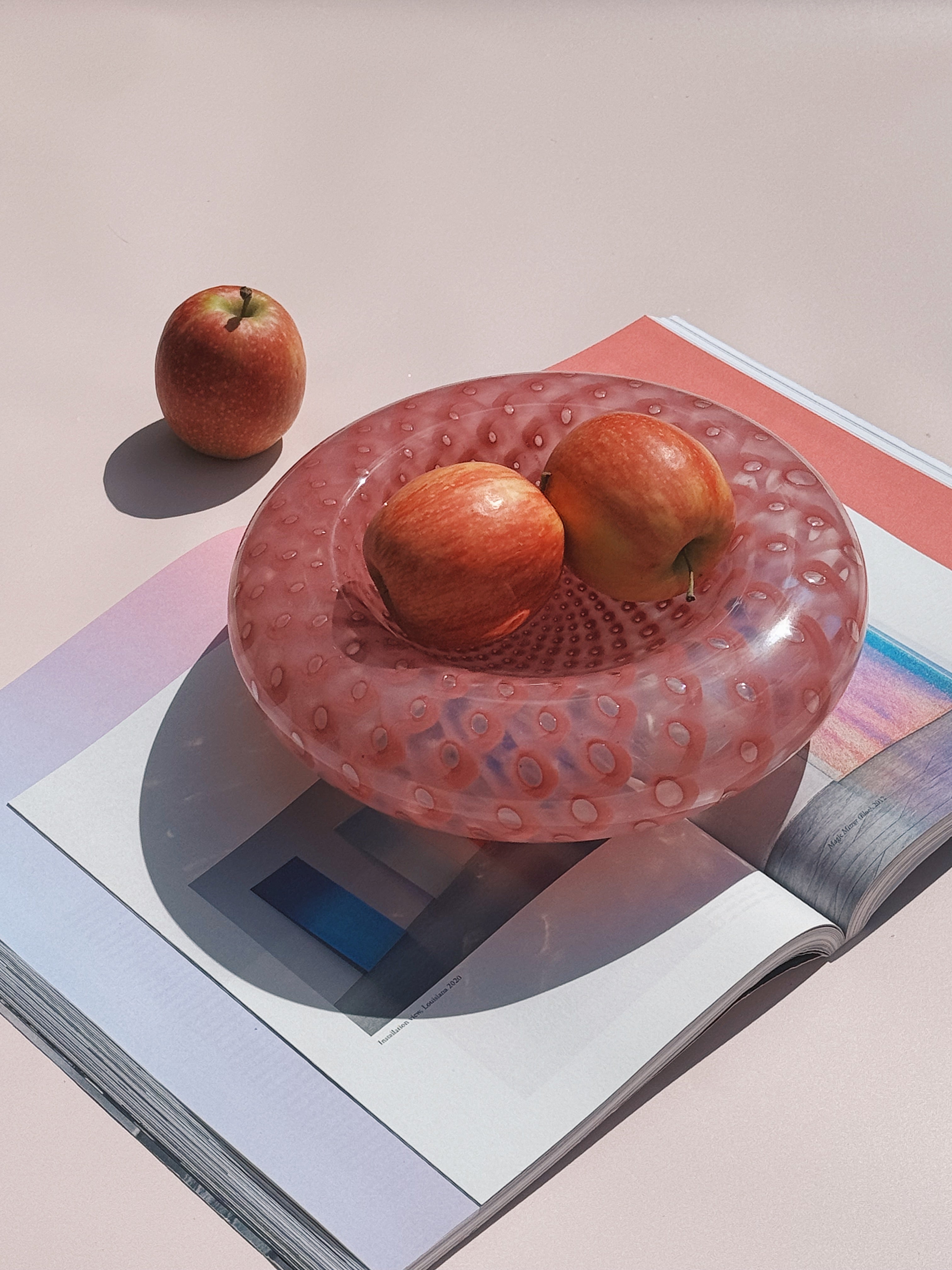 Pink Murano glass bowl with bubble design, styled with apples on a magazine in natural sunlight – Studio Hafnia