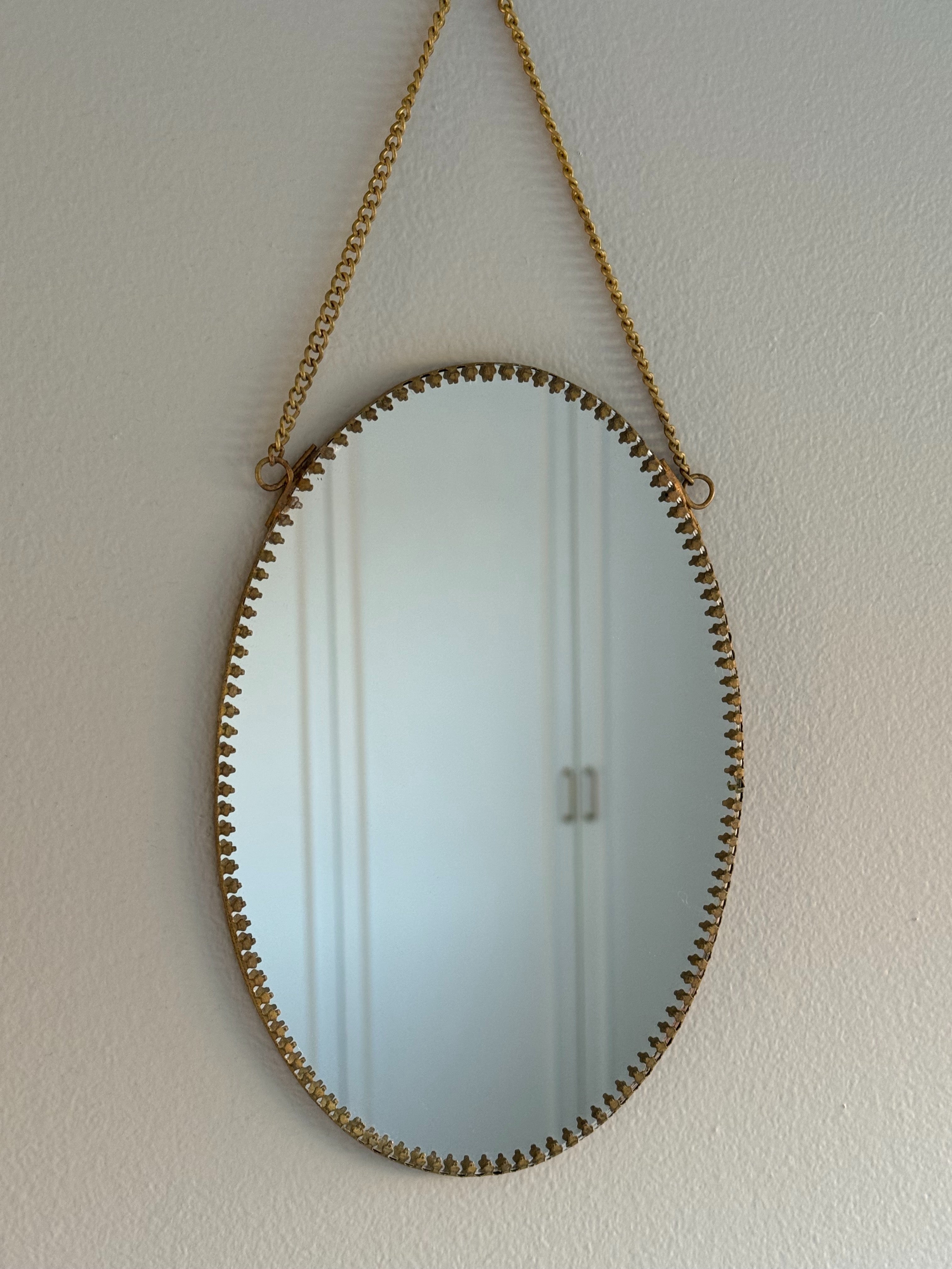 Vintage oval wall mirror with decorative brass frame and chain, hanging on a light-colored wall