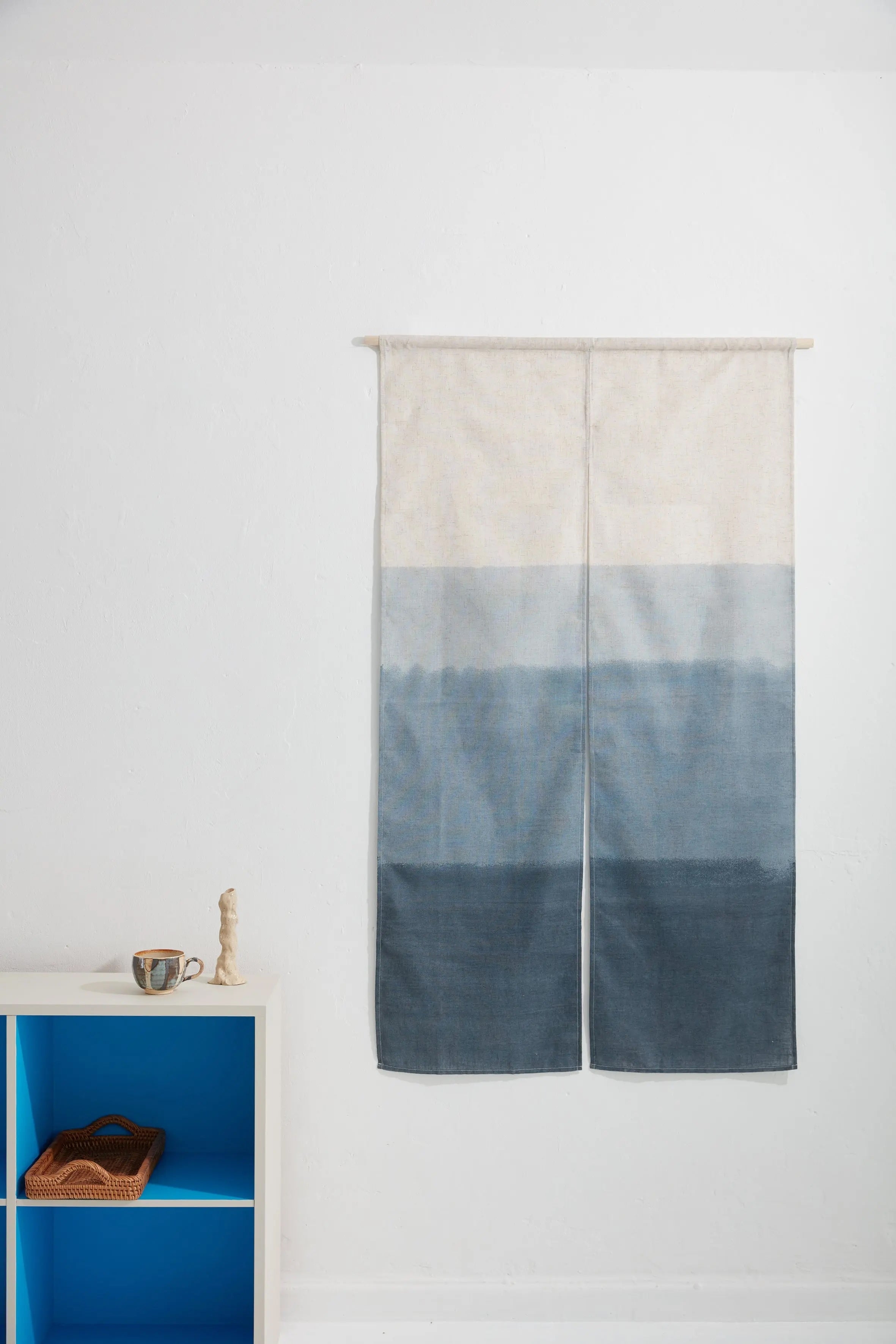 Japanese wall hanging in blue gradient design, displayed as textile art on a white wall with minimal interior styling
