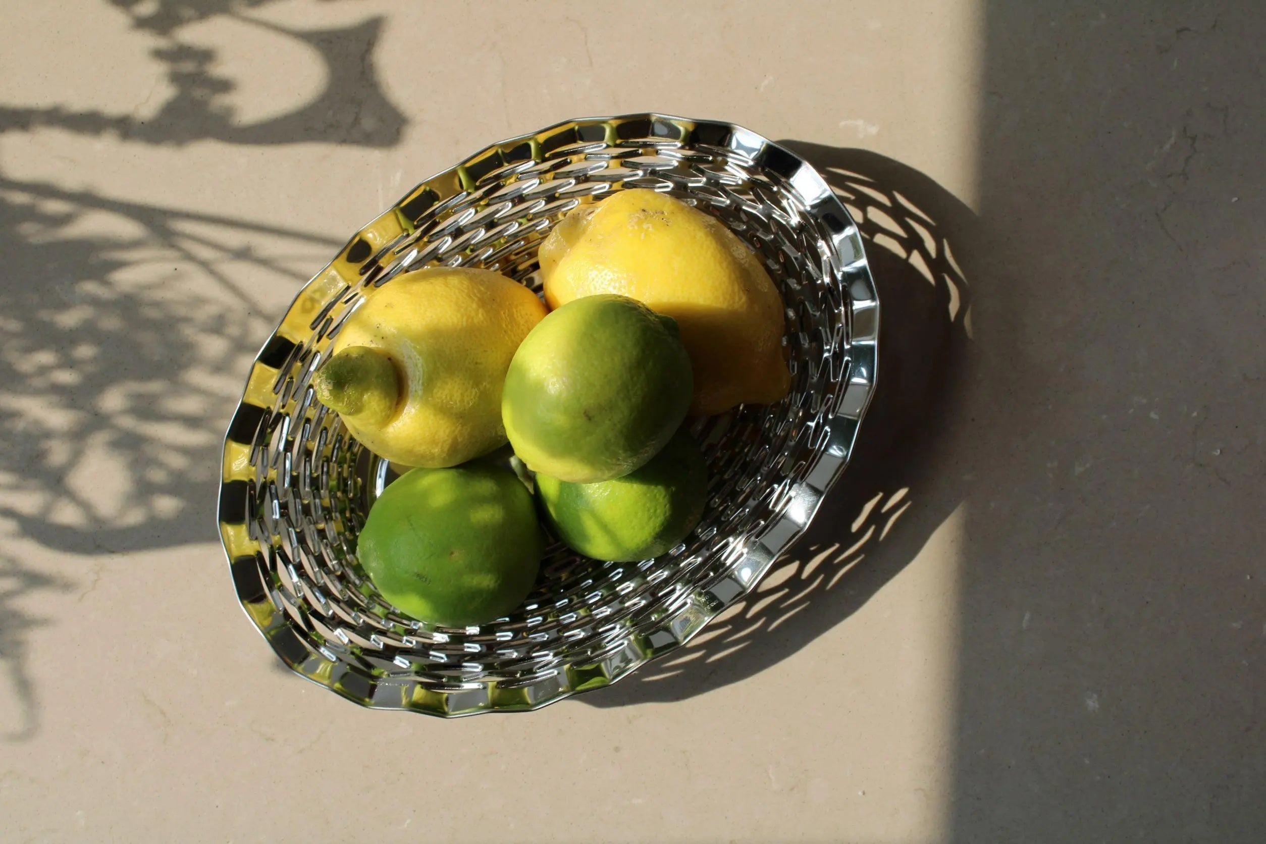 Oval stainless steel bread basket by Roger Orfevre with lemons and limes on a light surface