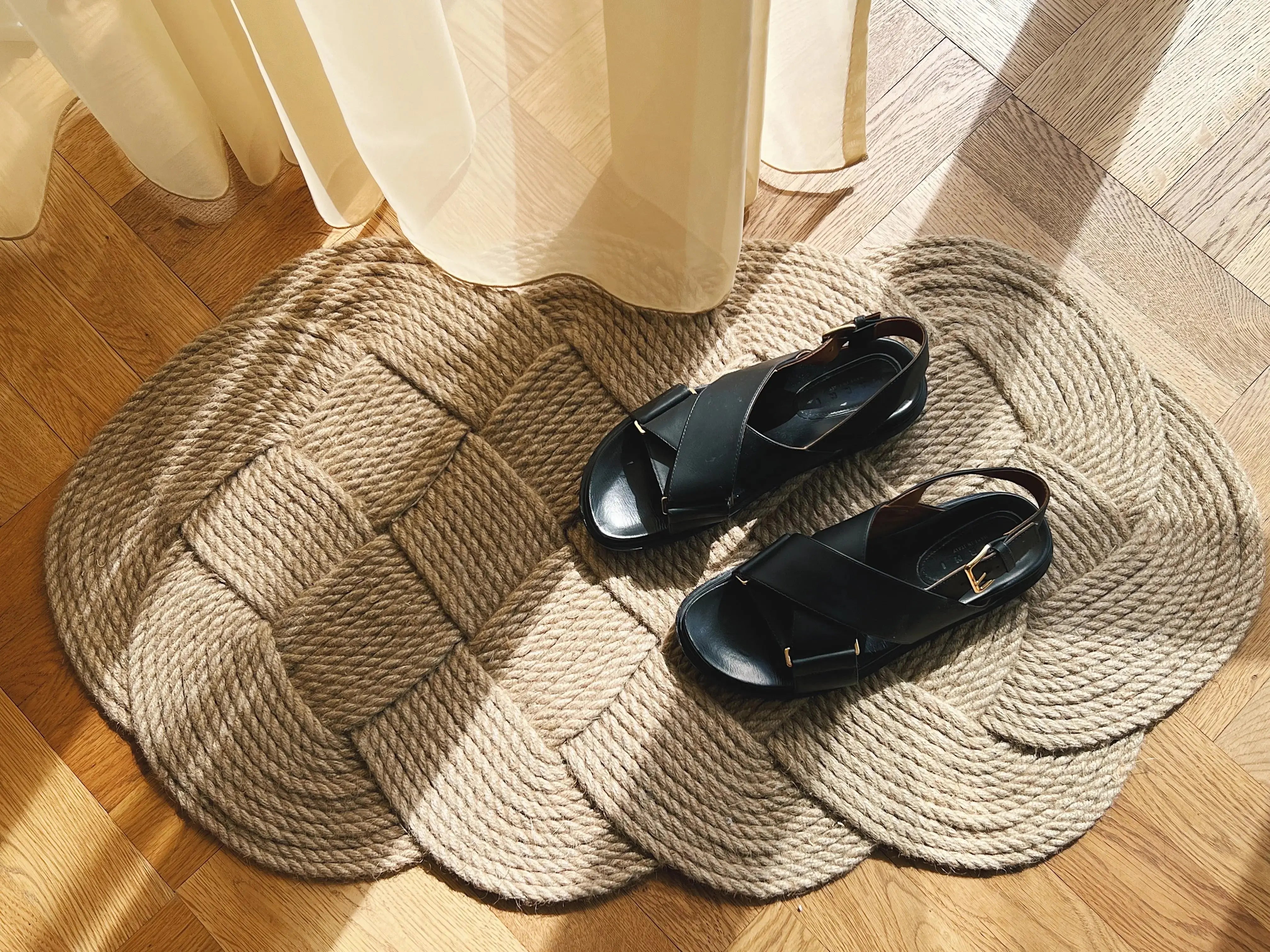 Original Ocean Plait doormat in handwoven natural jute, large size 50 x 93 cm, styled with black leather sandals on wooden floor.