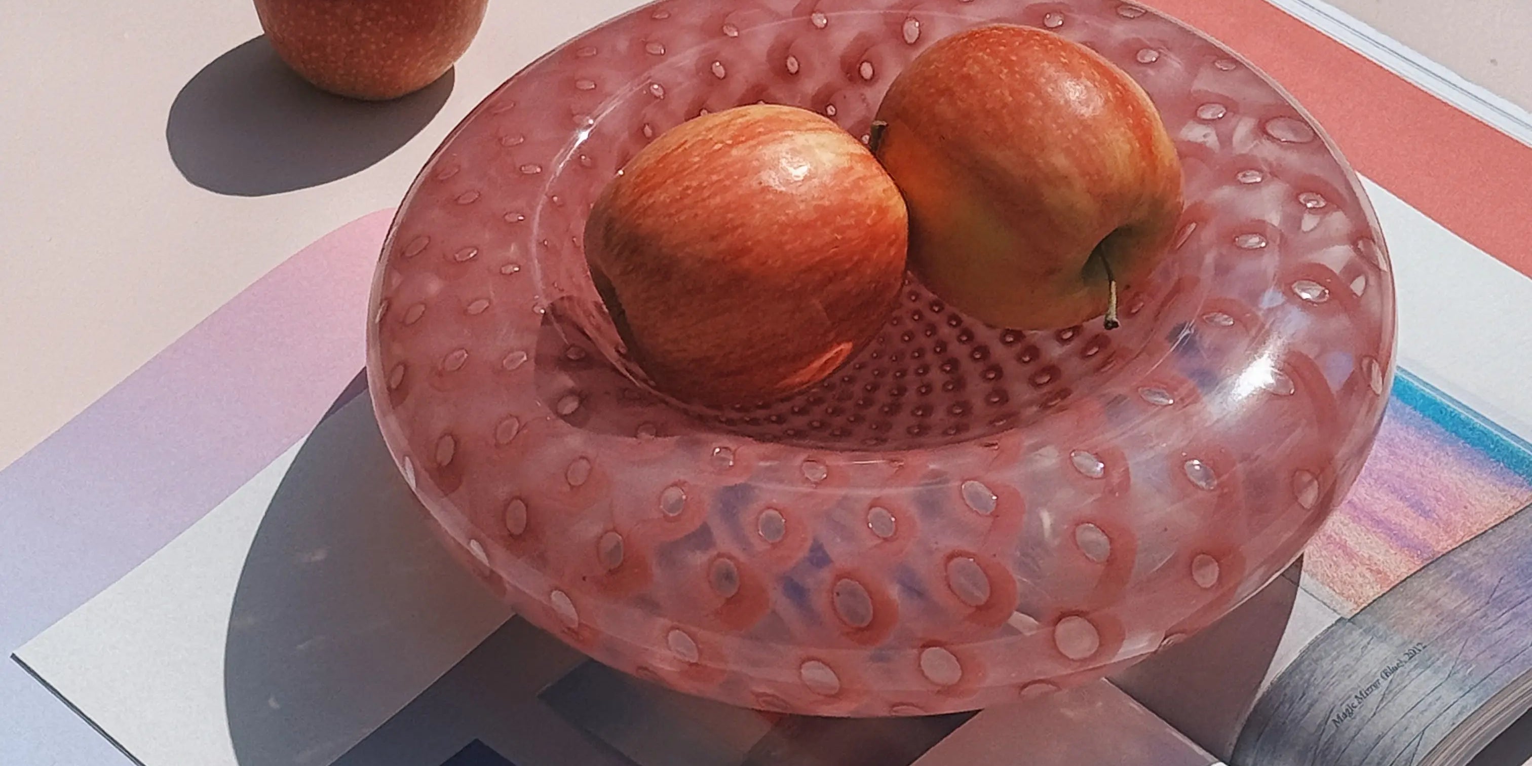 Pink Murano glass bowl with bubble design, styled with apples on a magazine in natural sunlight – Studio Hafnia