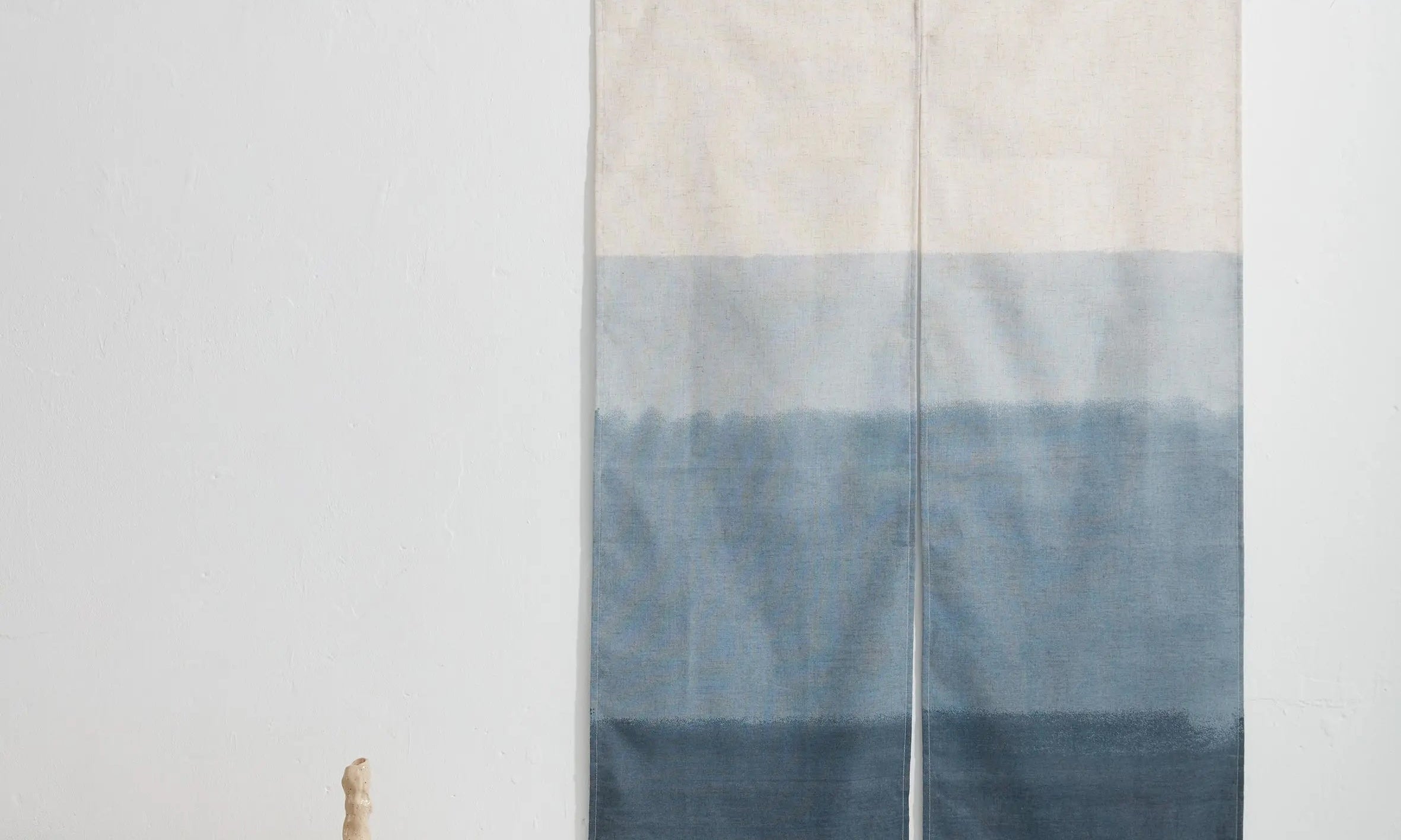 Japanese wall hanging in blue gradient design, displayed as textile art on a white wall with minimal interior styling