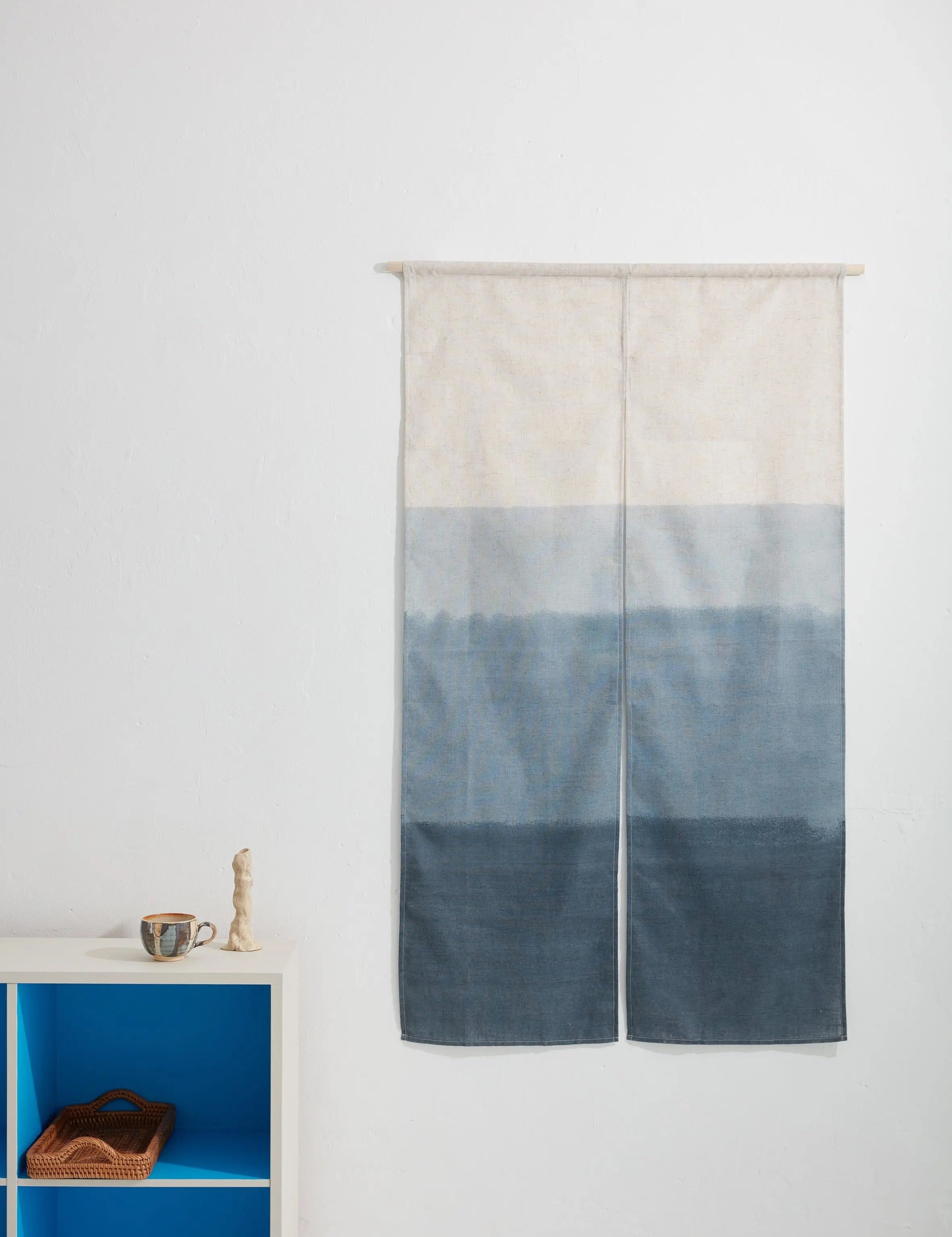 Japanese wall hanging in blue gradient design, displayed as textile art on a white wall with minimal interior styling