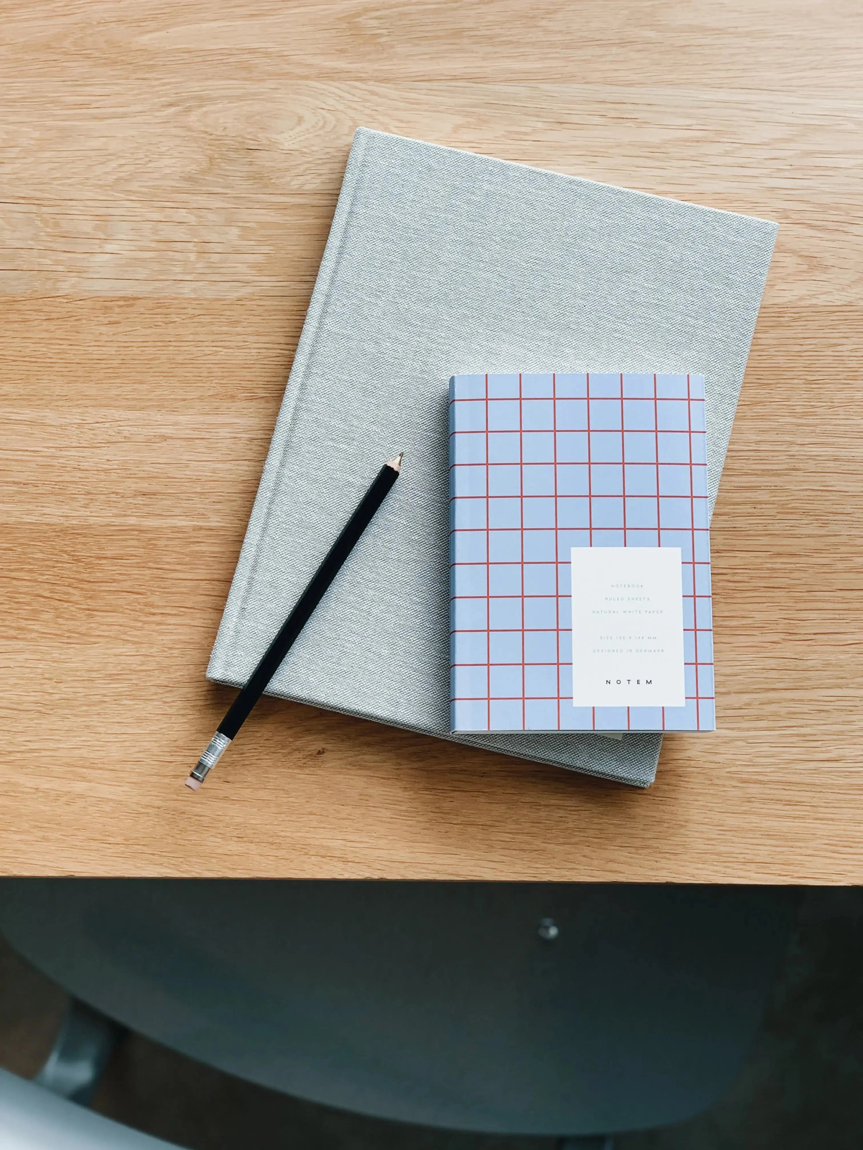 Flat lay of Notem Studio Uma notebook in light blue softcover, small size, styled with a pencil and grey notebook on wooden desk