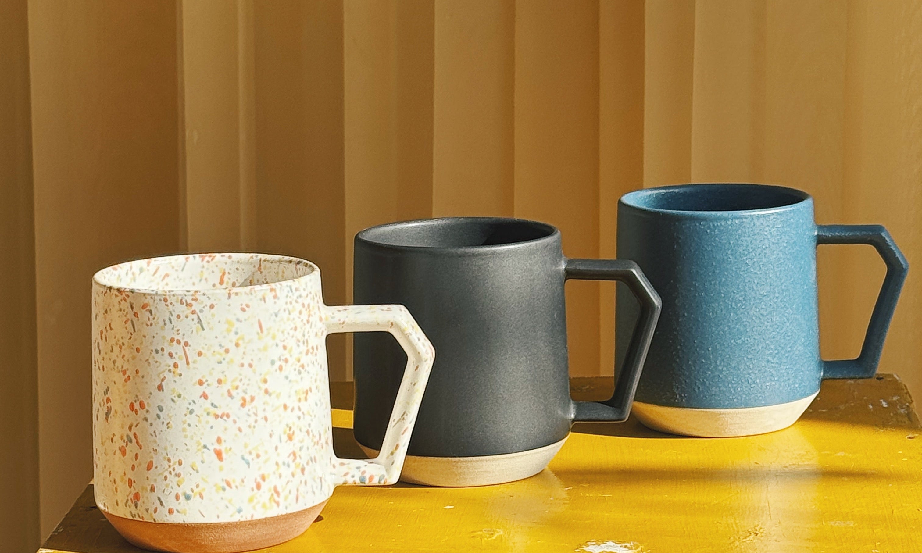 Three Chips Japan mugs in Minoyaki porcelain in different colors on a yellow chair – Japanese stackable cups available at Studio Hafnia.