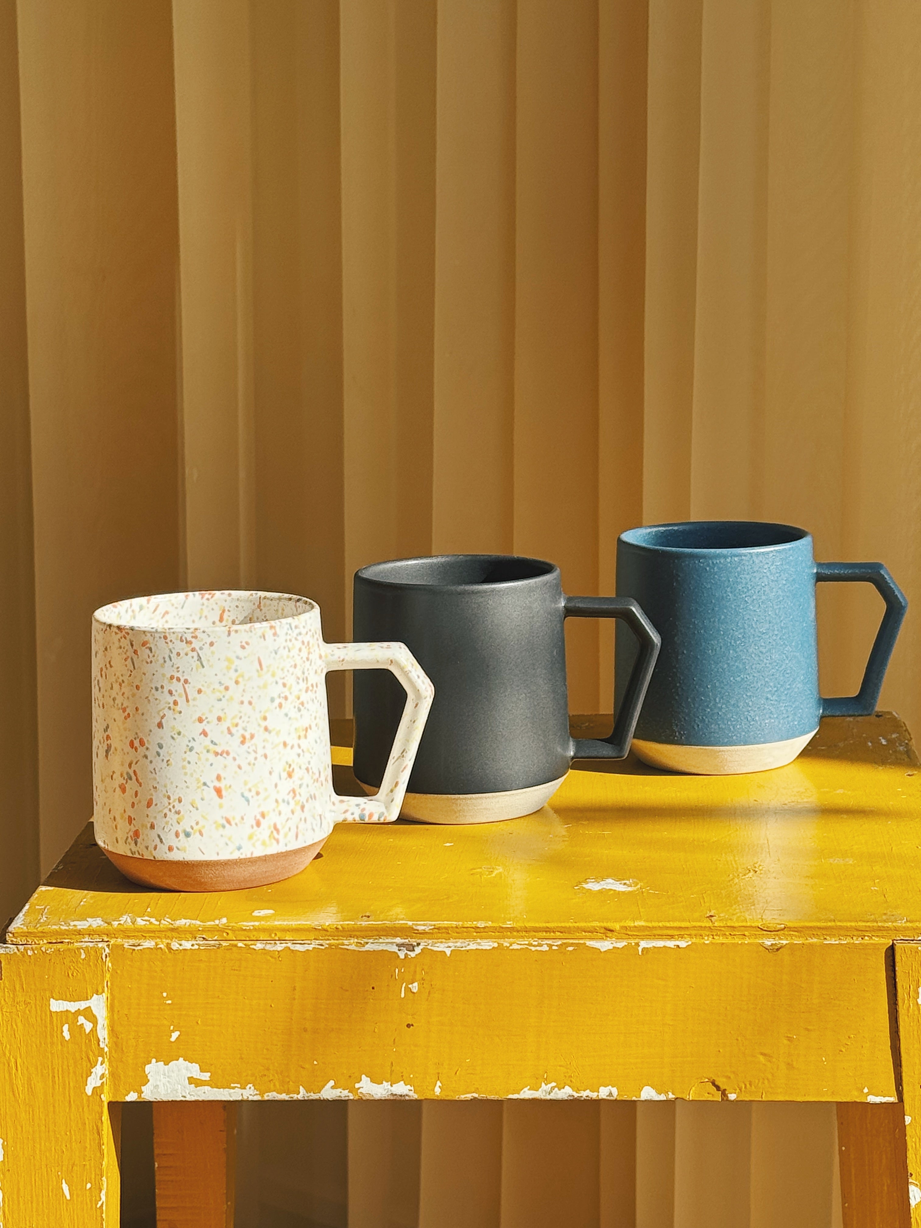 Three Chips Japan mugs in Minoyaki porcelain in different colors on a yellow chair – Japanese stackable cups available at Studio Hafnia.