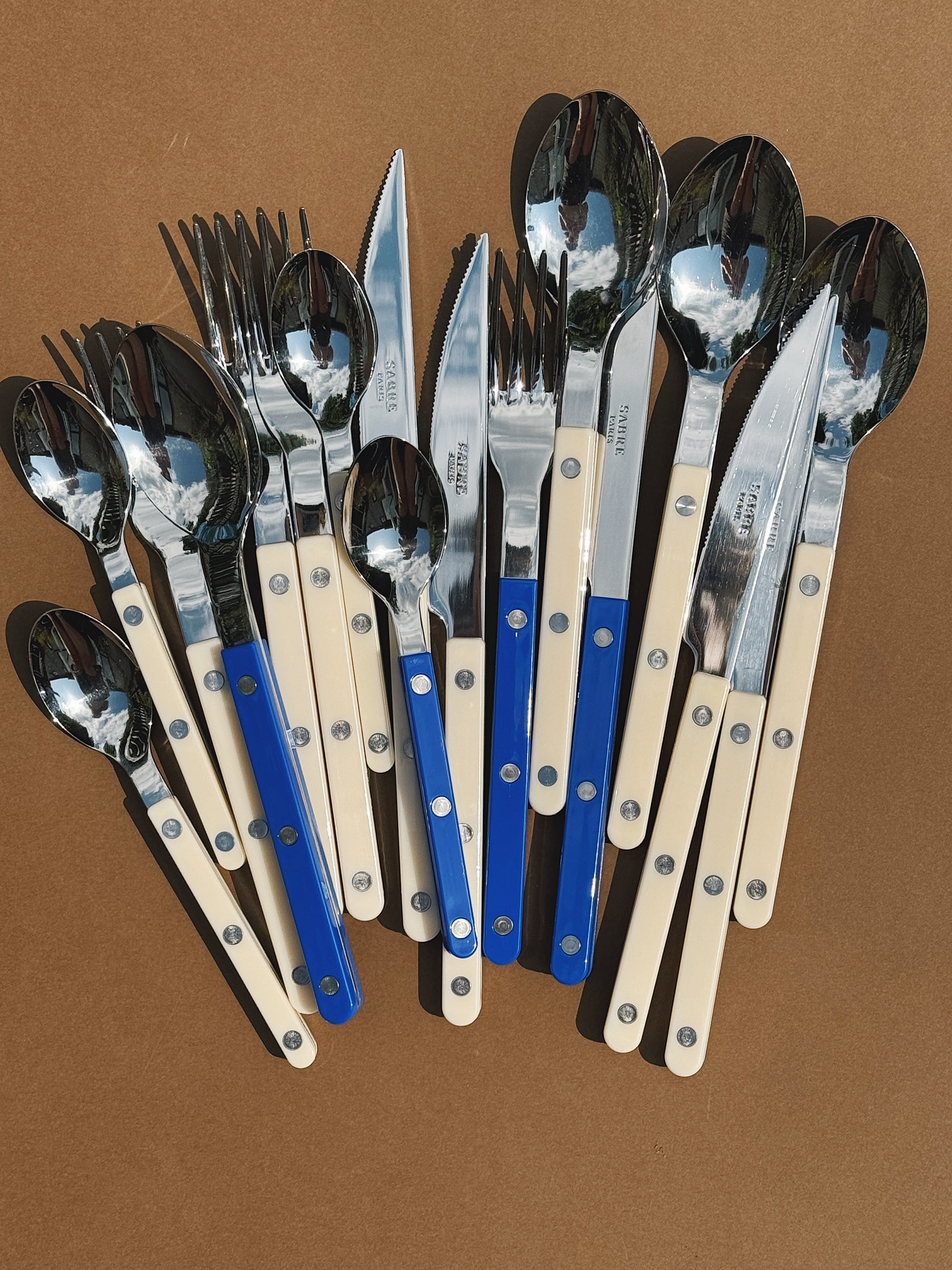 Sabre Paris Solid cutlery set in ivory and blue – forks, knives and spoons with French design handles displayed on brown background
