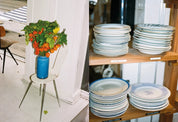 Tomato plant in a blue vase by the window and stacks of plates on wooden shelves at Atelier September