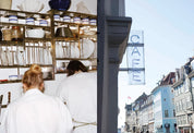Two staff in white behind the crockery shelf and a blue neon CAFE sign above a Copenhagen street