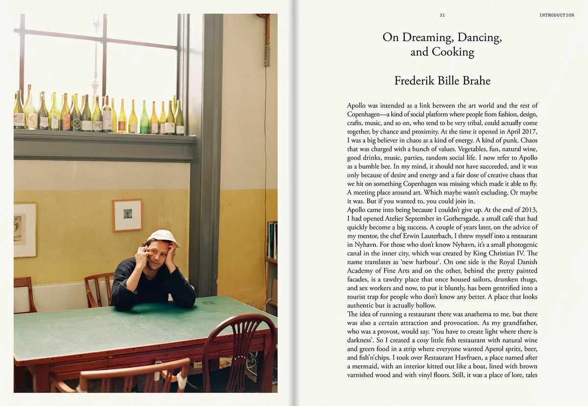 Frederik Bille Brahe at a green café table with wine bottles on the windowsill and the essay On Dreaming, Dancing, and Cooking