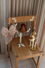 The five pieces of the Christmas package styled on an oak chair – hanging rattan bell, red and white striped bow, dove garland, silver candlestick and brass angel chime