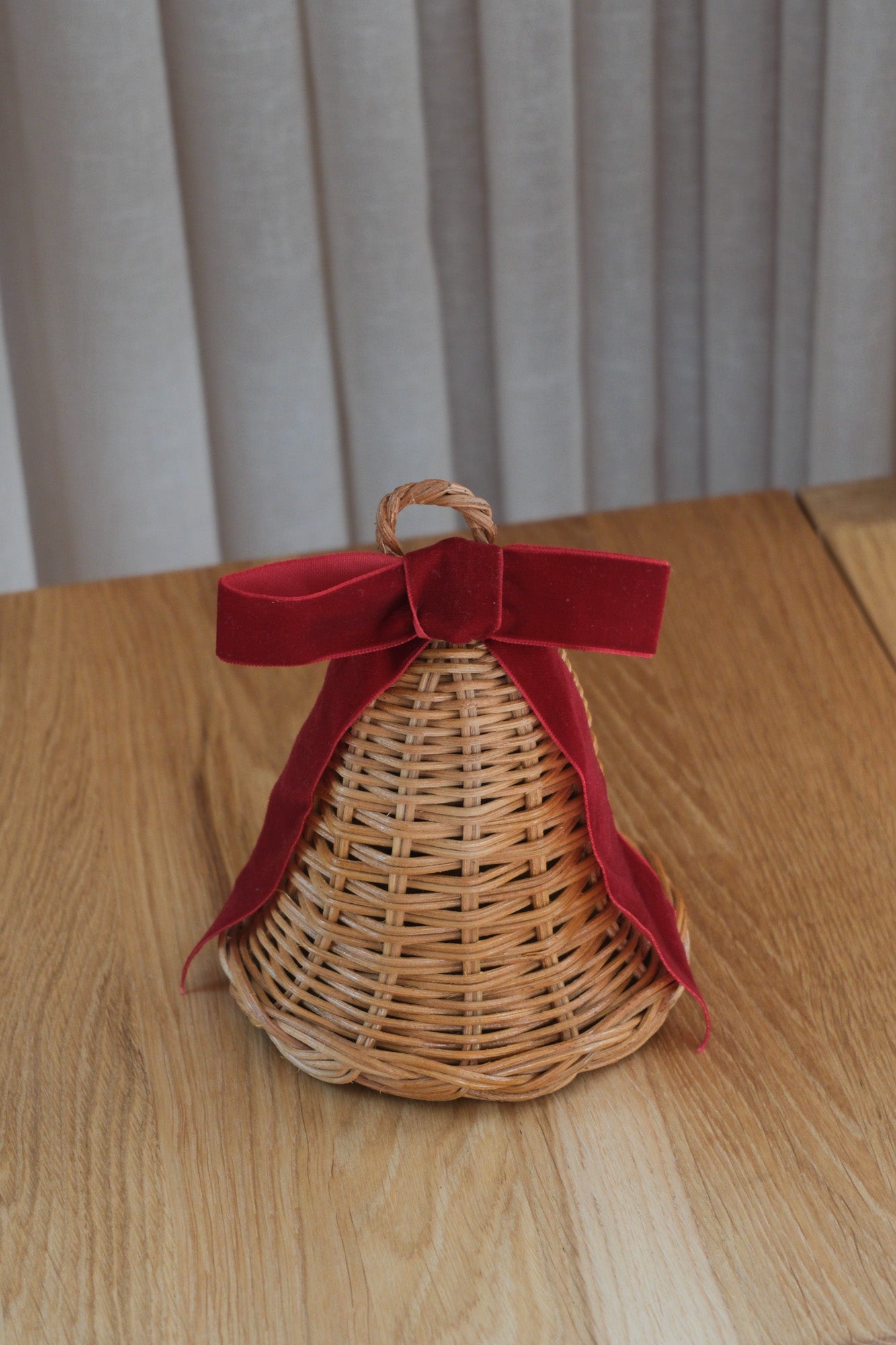 Standing rattan Christmas bell with deep red bow, 12.5 x 12.5 cm, on an oak table