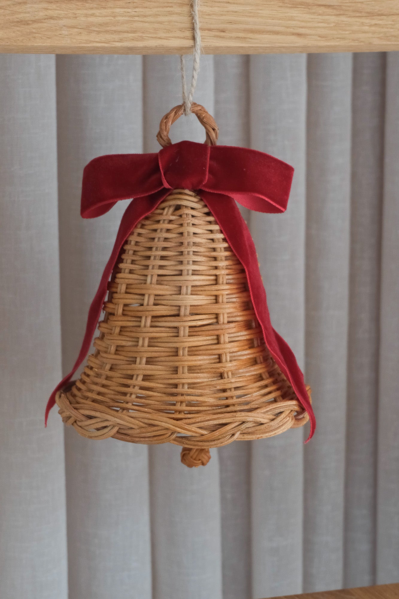 Rattan Christmas bell with deep red bow hanging from a cord