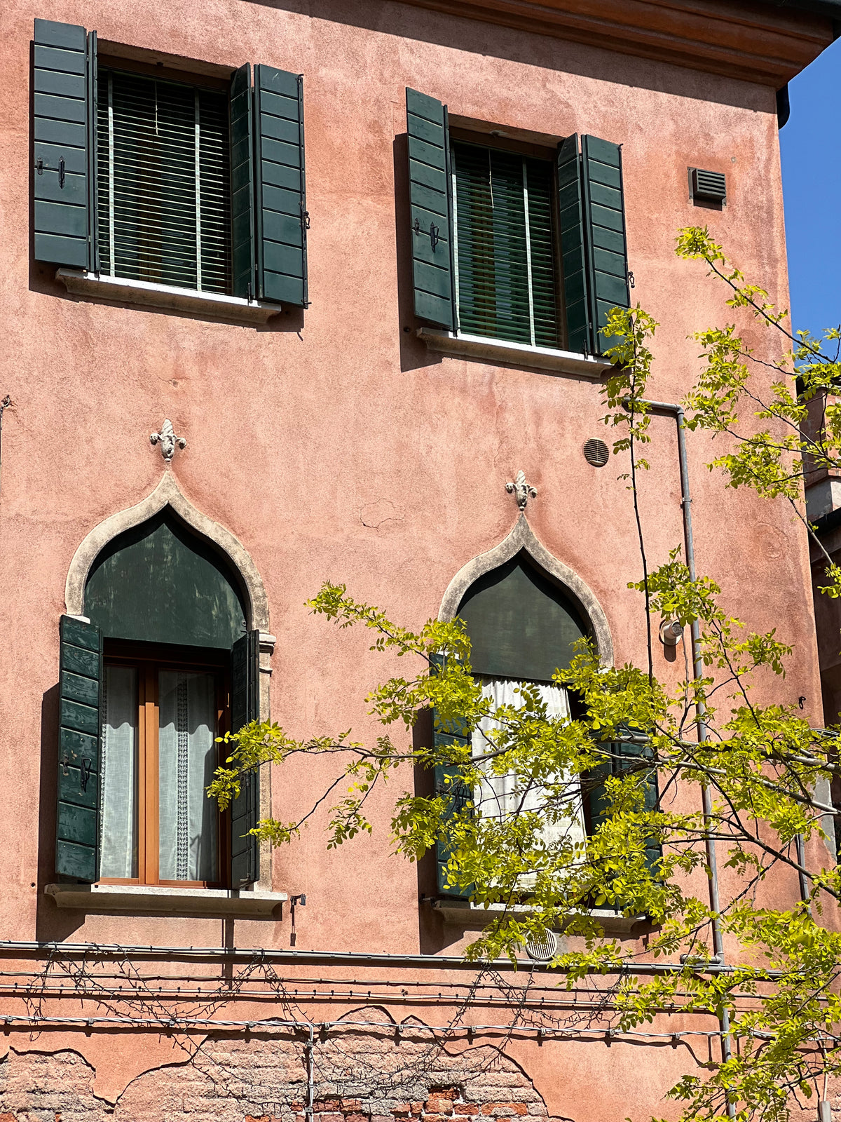 Venetiansk husfacade på Murano i rosa puds med gotiske spidsbuevinduer og grønne skodder