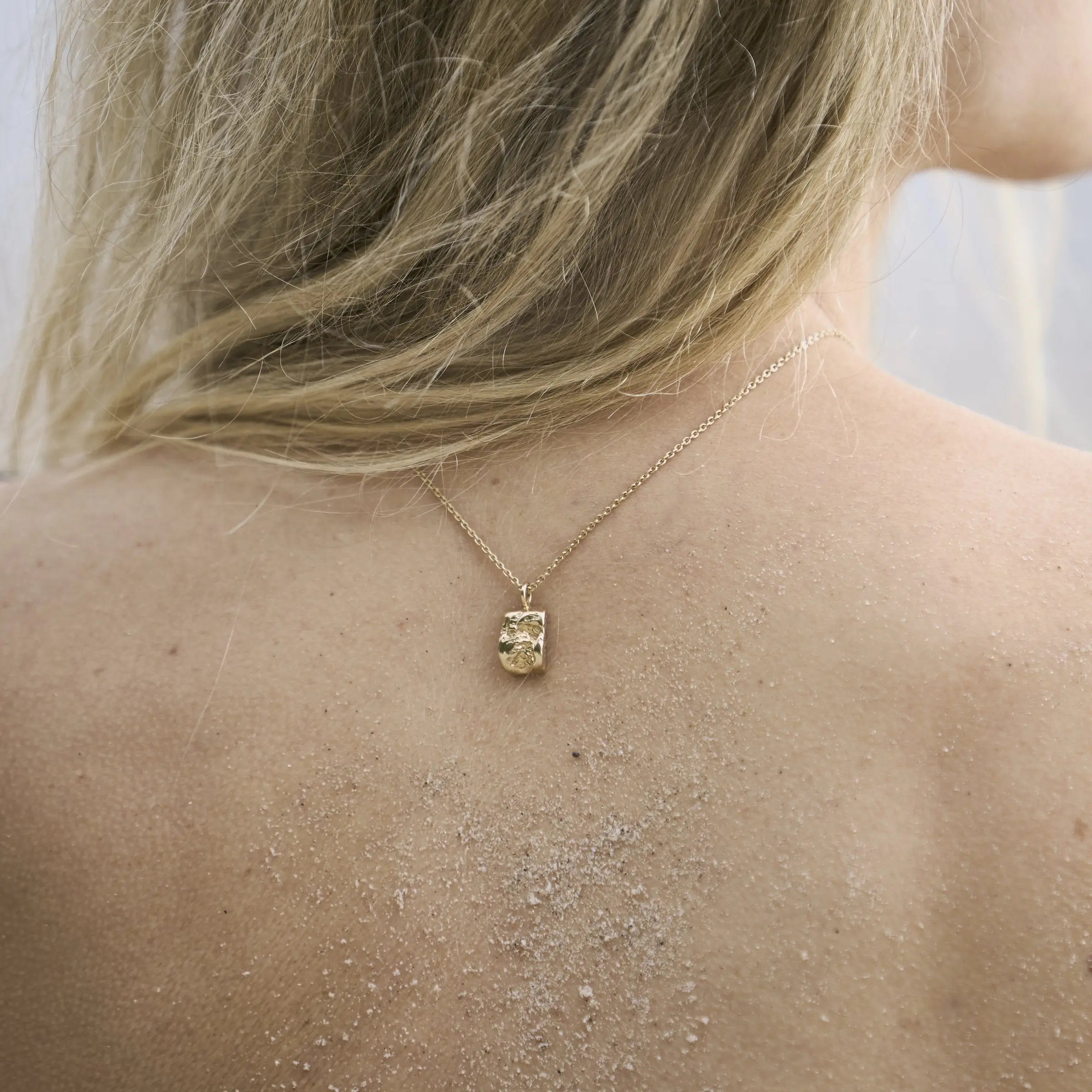 Close-up of the sculptural pendant on the Inger necklace in 14 carat gold against the skin