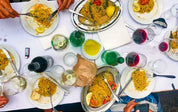 Long table seen from above with pasta dishes, wine and olive oil shared family style