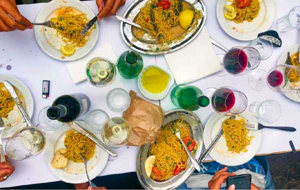 Long table seen from above with pasta dishes, wine and olive oil shared family style