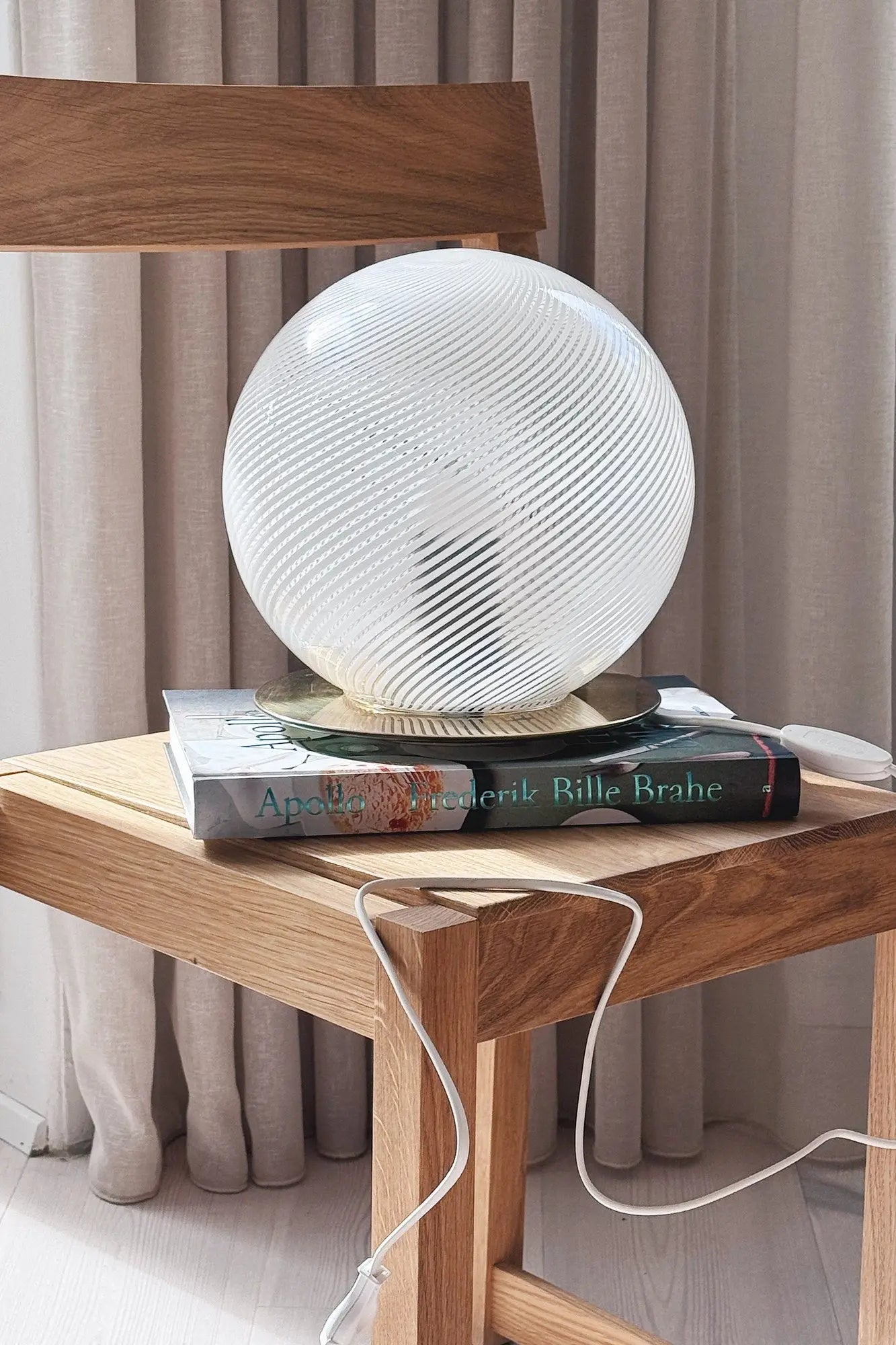 White Murano globe lamp H25 cm seen from the side on a stack of books on an oak chair