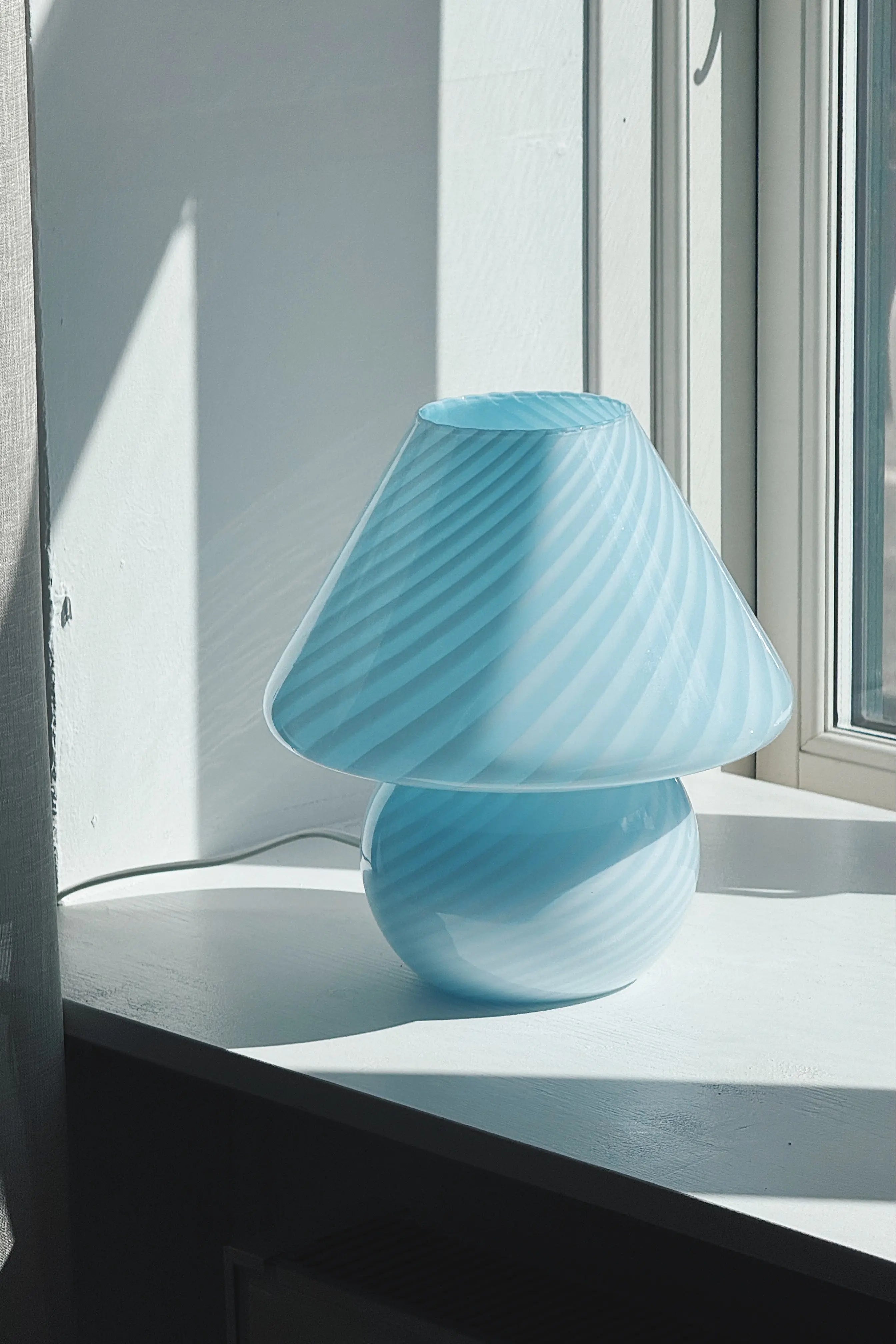 Light blue Murano mushroom table lamp seen from the side by a window in natural light