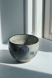 Japanese porcelain cup with purple camellia and brown rim seen from the side in window light, Ø 10 x H 7.2 cm
