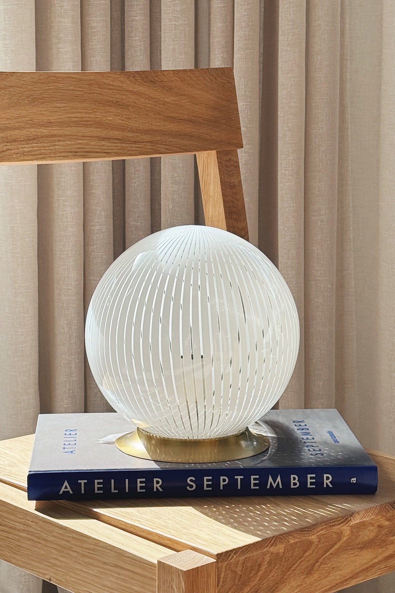 White Murano globe table lamp H20 cm styled in daylight on an oak chair with a book