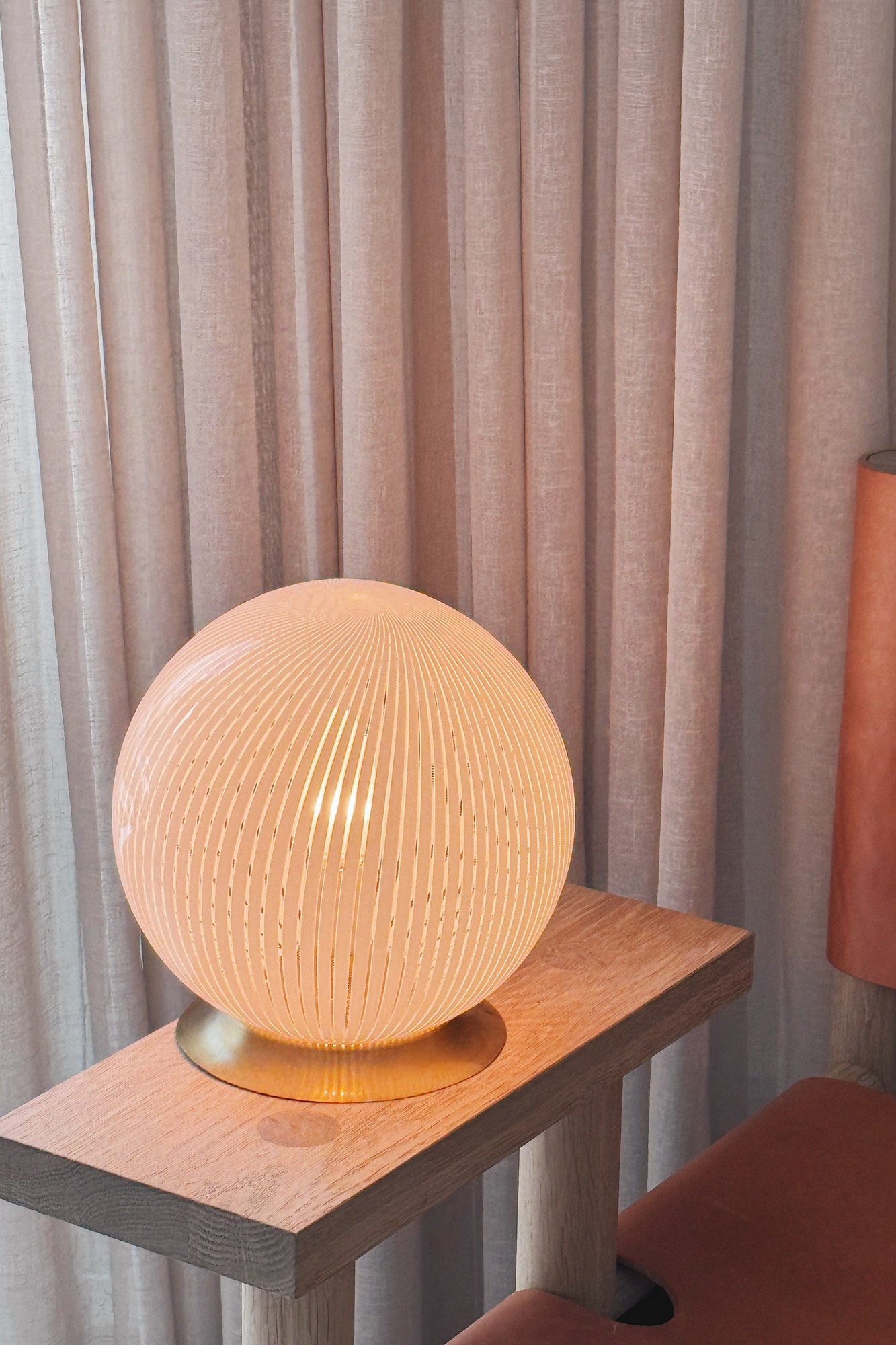 Lit vintage Murano filigrana globe table lamp in white glass giving a warm milky light, on an oak table