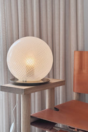 Murano globe table lamp switched on, the white swirl glass glowing softly on an oak table