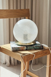 Murano globe table lamp in white swirl glass on books with the white cord running down the chair