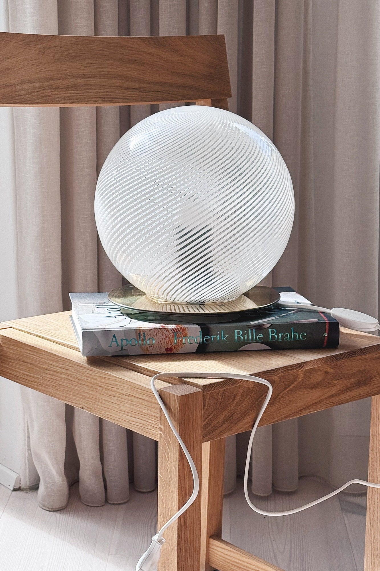 White Murano globe lamp H25 cm seen from the side on a stack of books on an oak chair