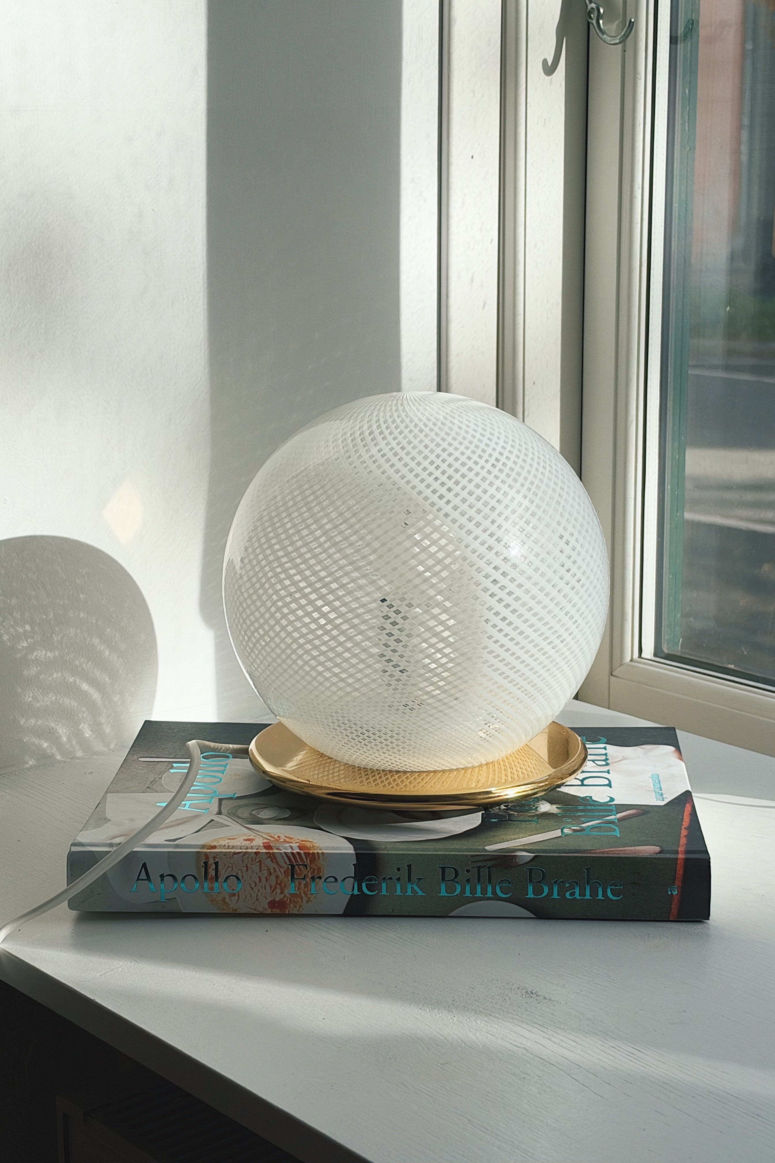 Hvid Murano globe bordlampe med fint diamantnet af hvide tråde, set forfra i modlys
